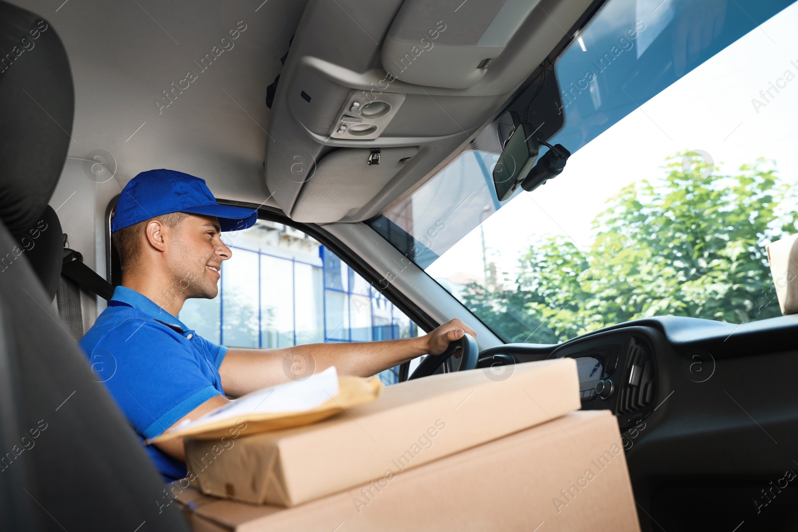 Photo of Young courier with parcels in delivery car