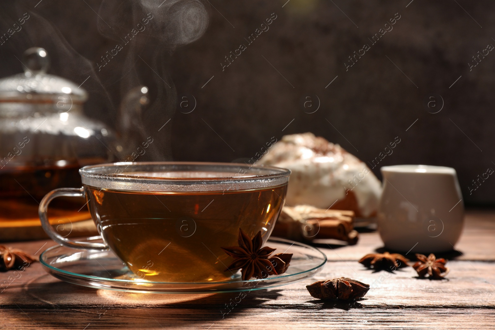 Photo of Glass cup of aromatic hot tea with anise stars on wooden table. Space for text