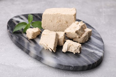 Photo of Pieces of tasty halva and mint served on light grey table, closeup