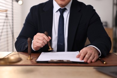 Photo of Notary stamping document at wooden table in office, closeup