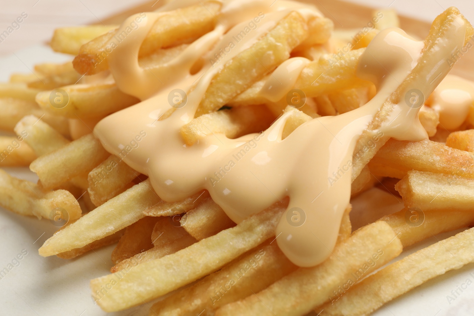 Photo of Delicious french fries with cheese sauce on board, closeup