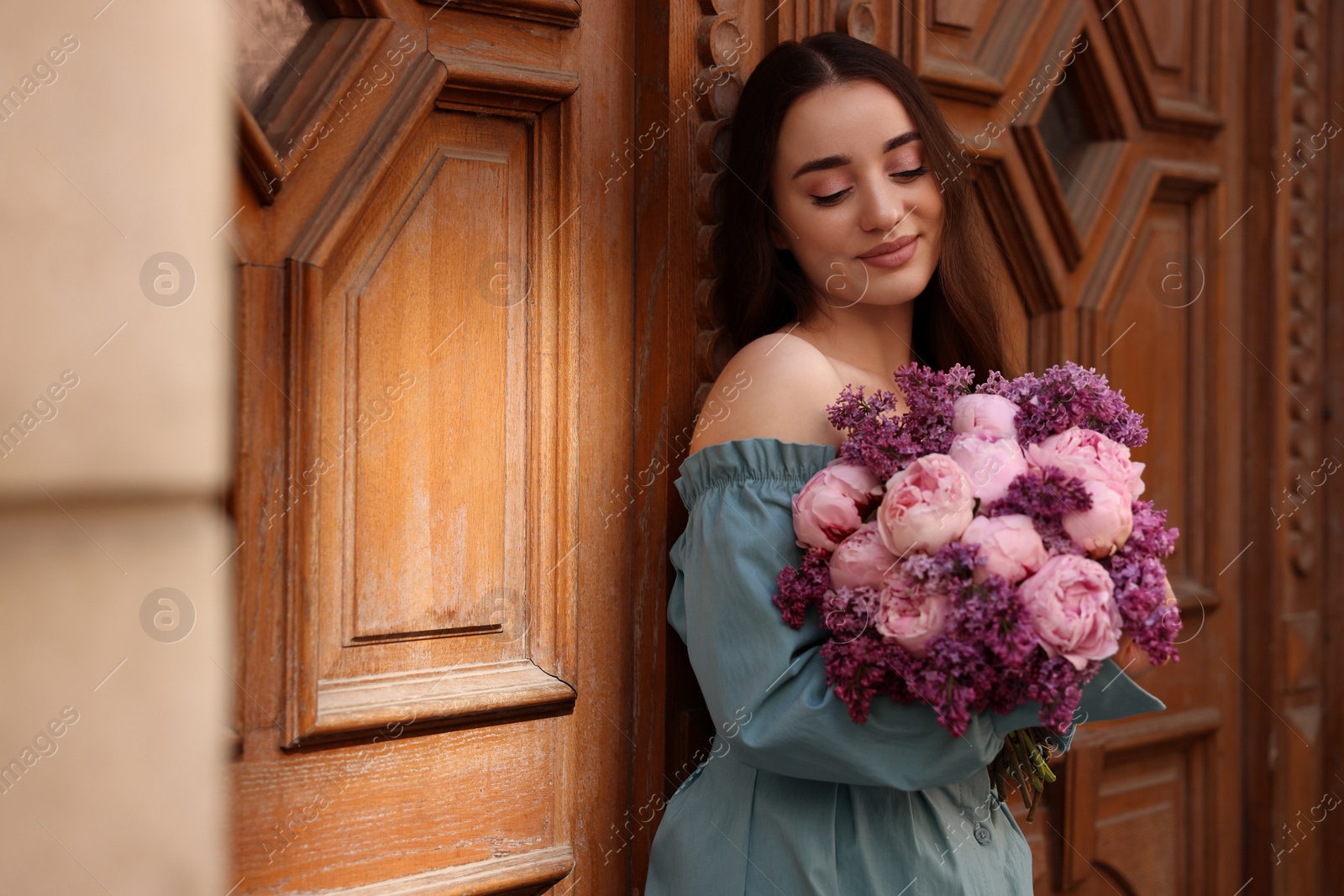 Photo of Beautiful woman with bouquet of spring flowers near building outdoors, space for text