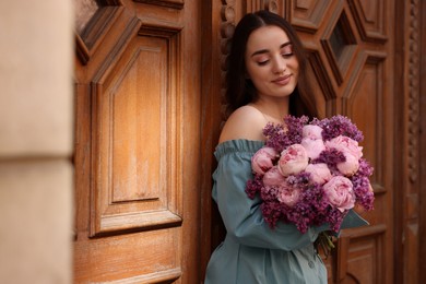 Beautiful woman with bouquet of spring flowers near building outdoors, space for text