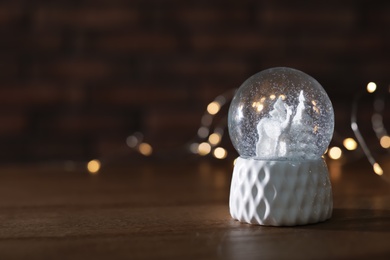 Snow globe with Christmas lights on wooden table. Space for text