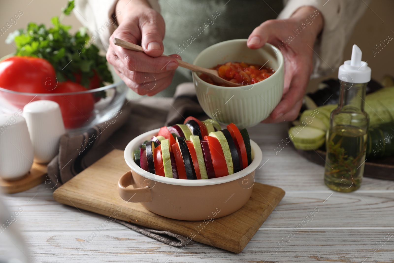 Photo of Cooking delicious ratatouille. Woman dressing fresh vegetables in bowl at white wooden table, closeup