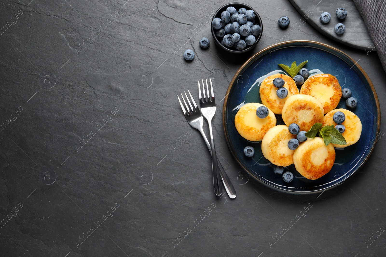 Photo of Delicious cottage cheese pancakes with blueberries on black table, flat lay. Space for text
