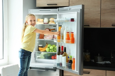 Photo of Girl taking bottle with juice out of refrigerator in kitchen