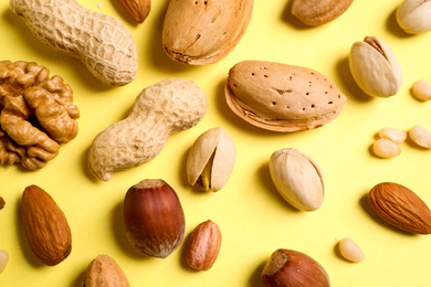 Different delicious nuts on yellow background, flat lay