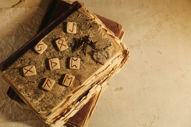 Photo of Wooden runes and old books on beige table, top view. Space for text