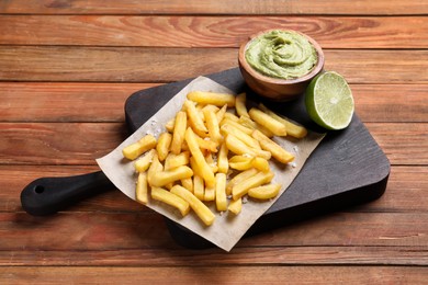 Photo of Serving board with french fries, avocado dip and lime served on wooden table