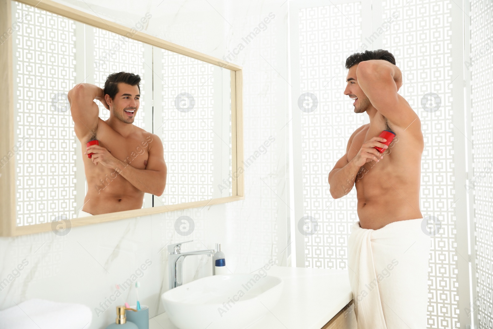 Photo of Handsome young man applying deodorant in bathroom