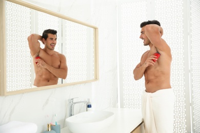 Handsome young man applying deodorant in bathroom