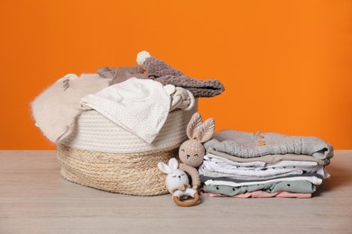 Laundry basket with baby clothes and crochet toys on wooden table against orange background