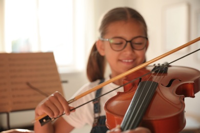 Photo of Cute little girl playing violin indoors. Music lesson, focus on strings