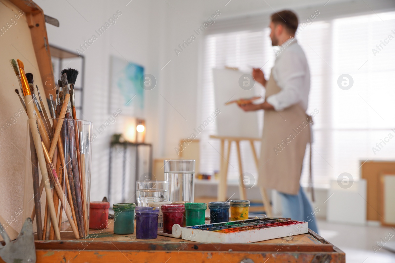 Photo of Young man painting with brush in artist studio, focus on tools