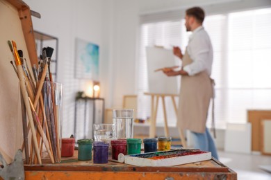 Young man painting with brush in artist studio, focus on tools