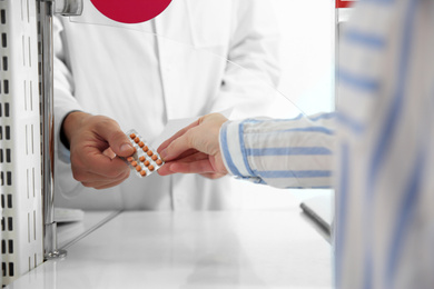 Image of Professional pharmacist giving pills to customer in drugstore, closeup