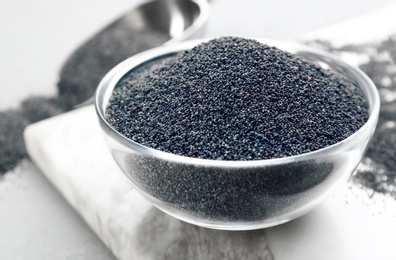 Photo of Poppy seeds in bowl on white marble board, closeup