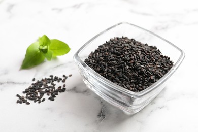 Photo of Black sesame seeds and green leaf on white marble table, closeup
