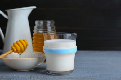 Photo of Glass with milk and jar of honey on grey wooden table. Space for text