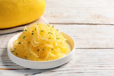 Photo of Plate with cooked spaghetti squash on wooden table. Space for text