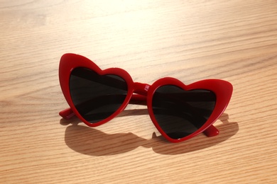 Stylish heart shaped sunglasses on wooden background