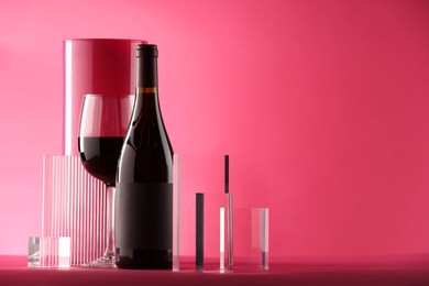 Photo of Stylish presentation of delicious red wine in bottle and glass on pink background. Space for text