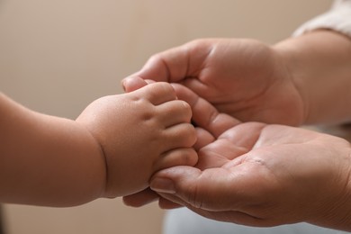 Photo of Woman holding hands with her granddaughter on beige background, closeup