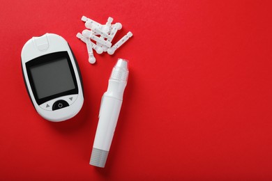 Digital glucometer, lancets and pen on red background, flat lay with space for text. Diabetes control