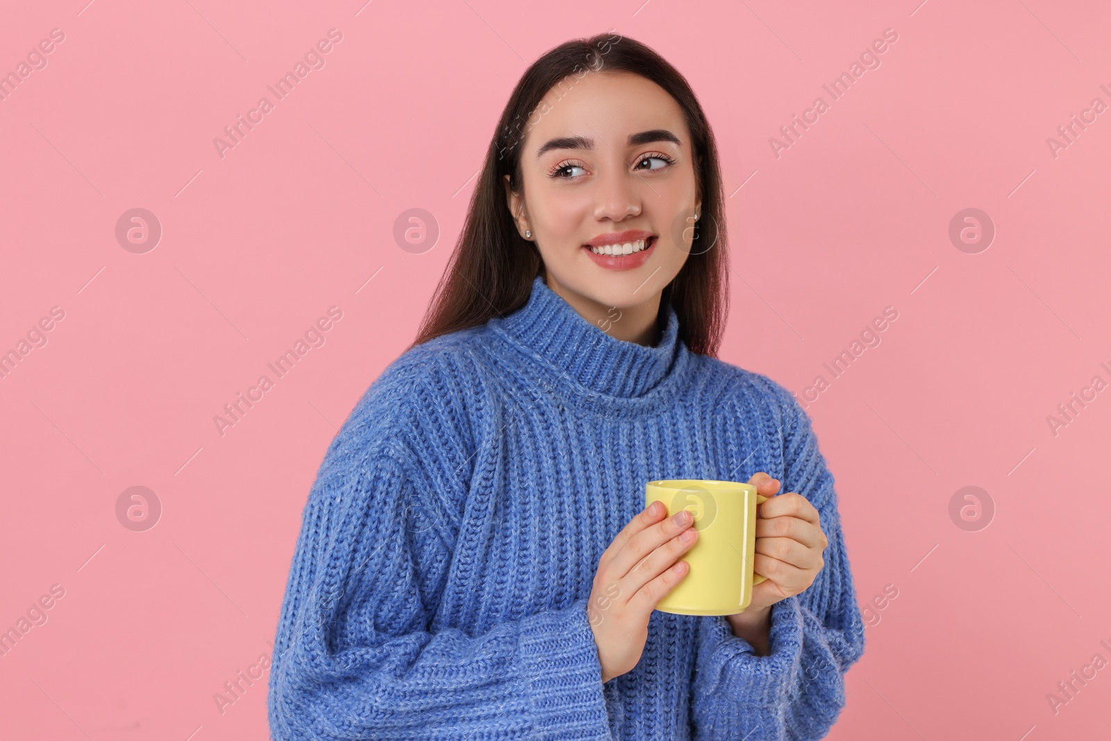 Photo of Happy young woman holding yellow ceramic mug on pink background