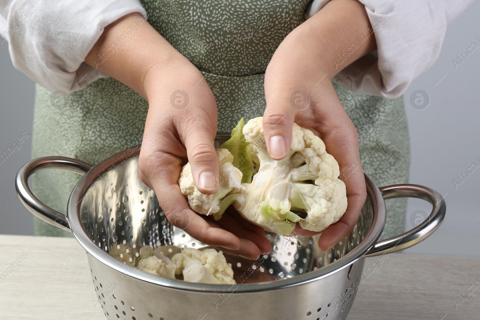 Photo of Woman separating fresh cauliflower cabbage above colander at wooden table, closeup