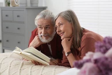 Photo of Lovely senior couple reading book on bed at home