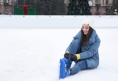 Image of Woman adjusting figure skate while sitting on ice rink. Space for text