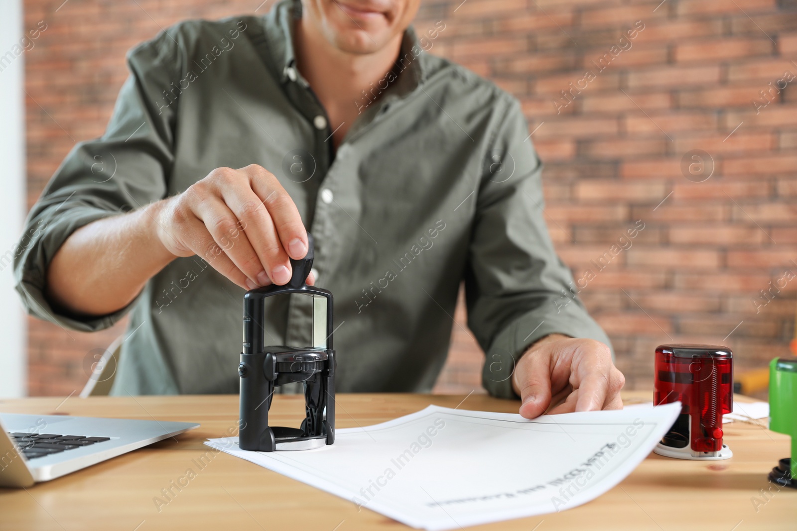 Photo of Male notary stamping document at table in office, closeup