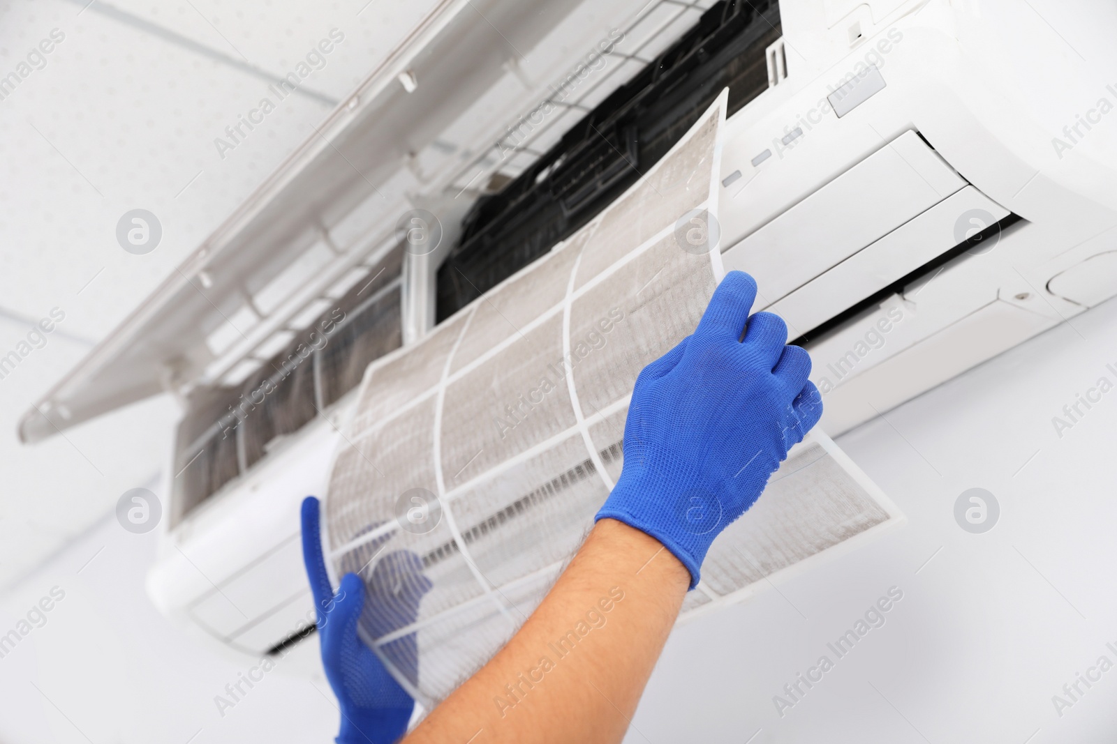 Photo of Professional technician maintaining modern air conditioner indoors, closeup