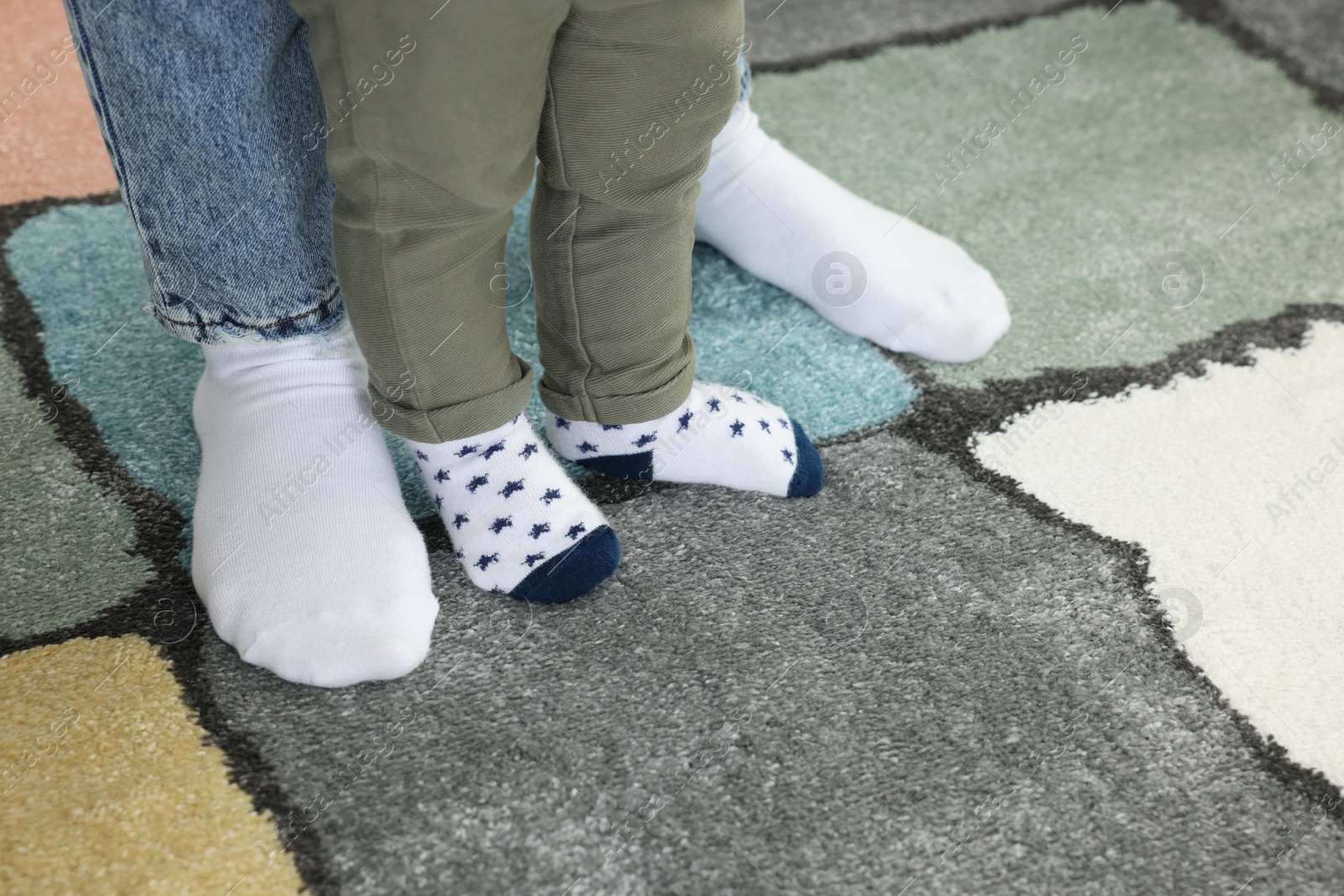 Photo of Mother supporting her son while he learning to walk on carpet, closeup. Space for text