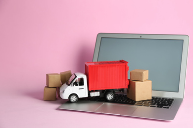 Photo of Laptop, truck model and carton boxes on pink background. Courier service