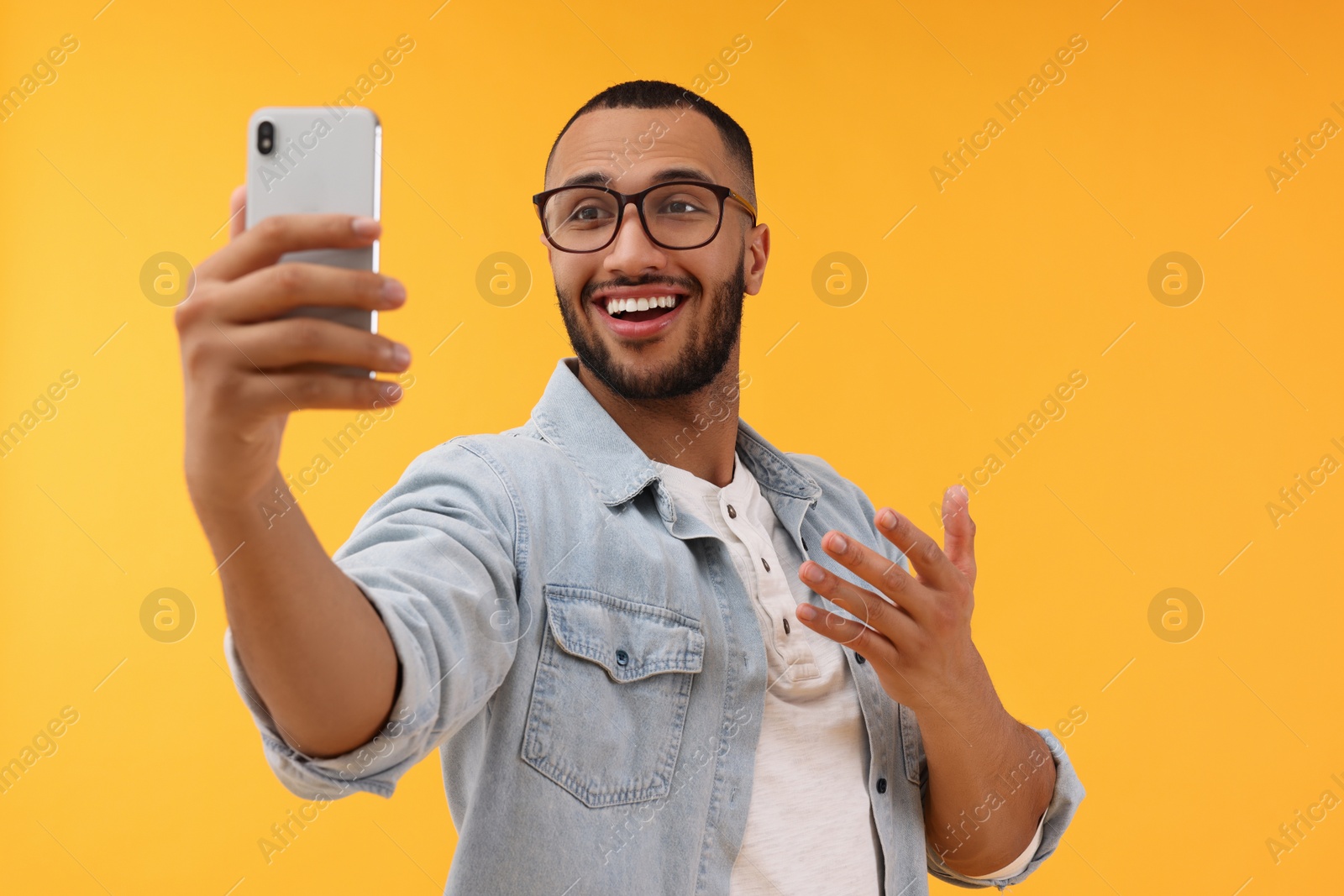 Photo of Smiling young man taking selfie with smartphone on yellow background