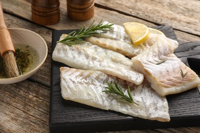 Fresh raw cod fillets with rosemary and lemon on wooden table, closeup