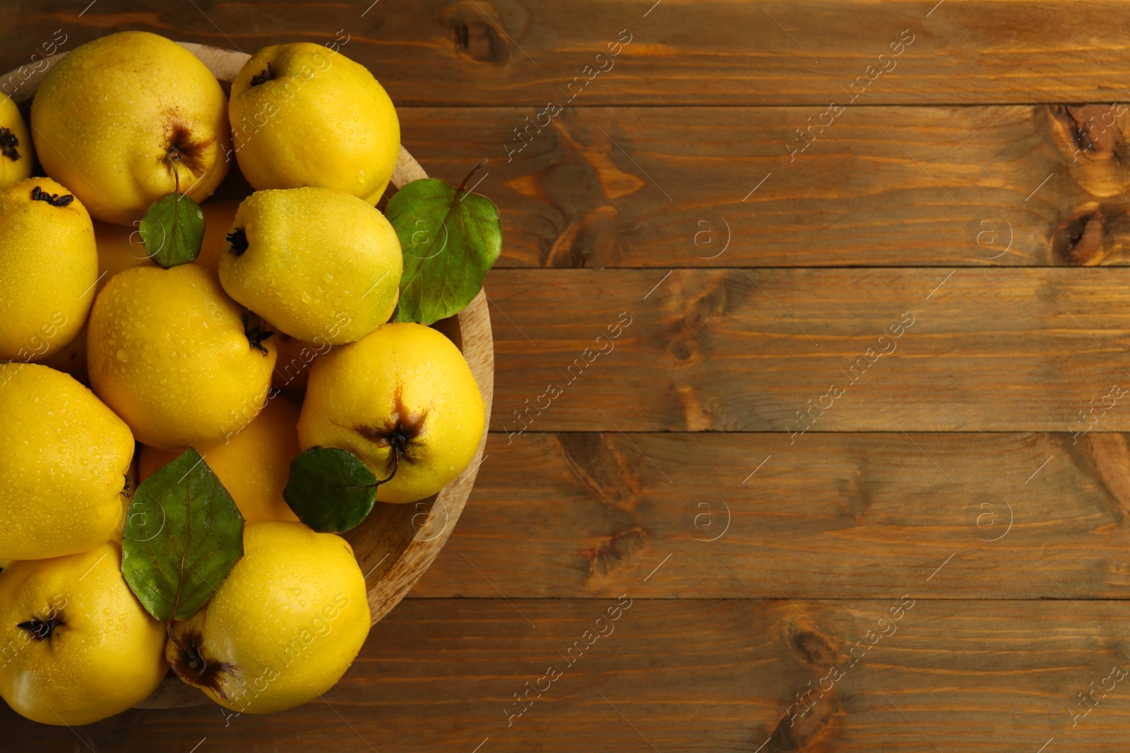 Photo of Tasty ripe quince fruits with water drops in bowl on wooden table, top view. Space for text