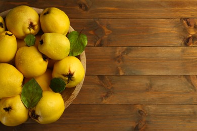 Photo of Tasty ripe quince fruits with water drops in bowl on wooden table, top view. Space for text