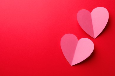 Pink paper hearts on red background, flat lay. Space for text