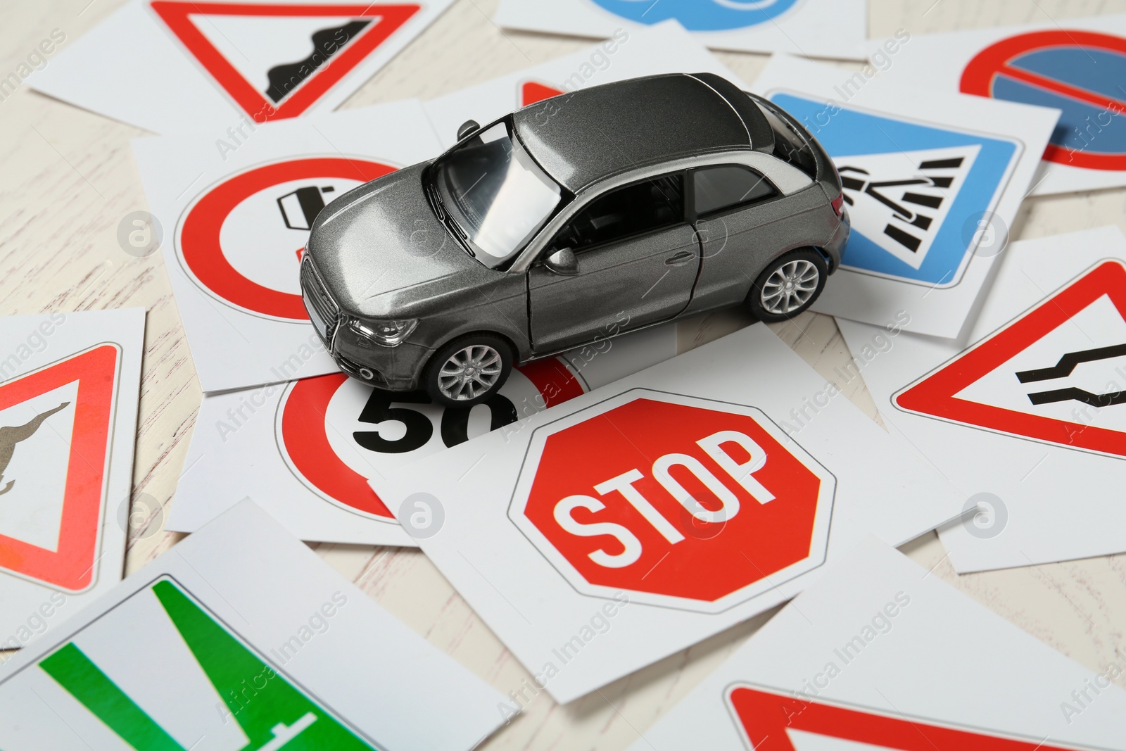 Photo of Cards with different road signs and toy car on white wooden table. Driving school