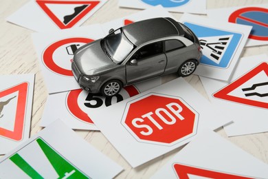 Photo of Cards with different road signs and toy car on white wooden table. Driving school