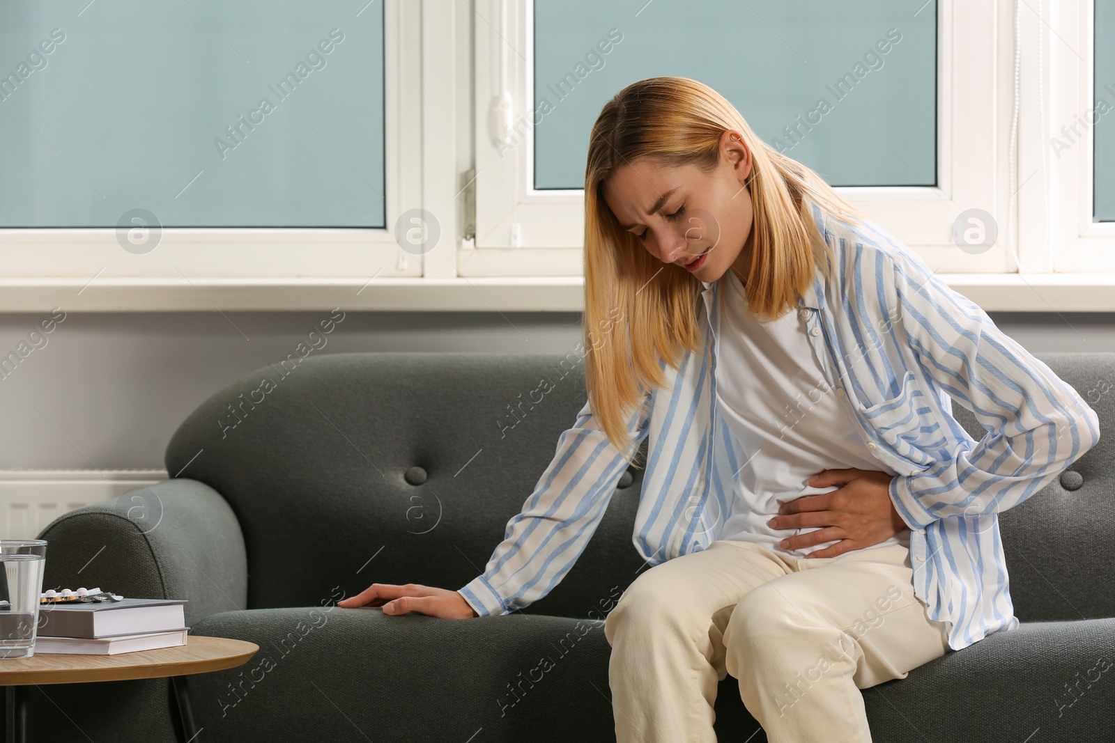 Photo of Young woman suffering from menstrual pain on sofa indoors