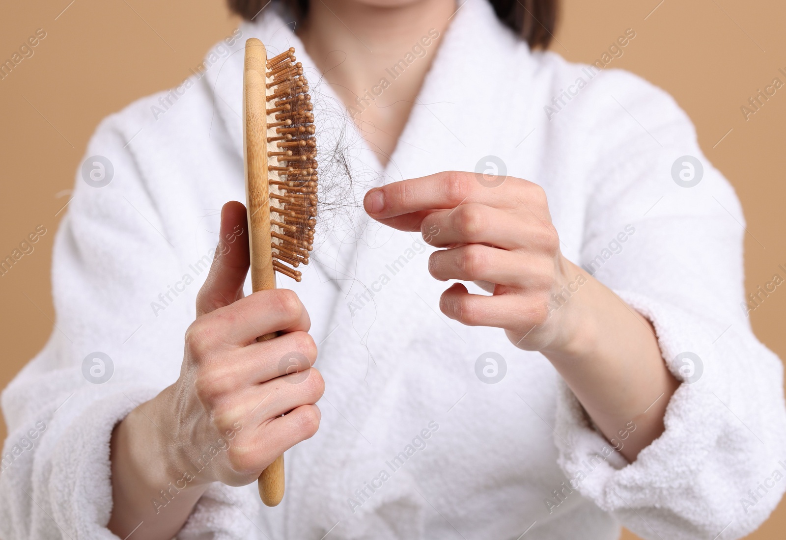 Photo of Woman taking her lost hair from brush on light brown background, closeup. Alopecia problem