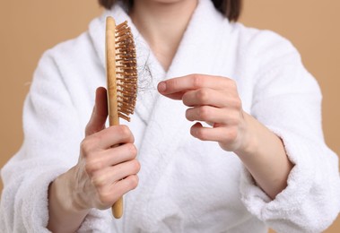 Woman taking her lost hair from brush on light brown background, closeup. Alopecia problem