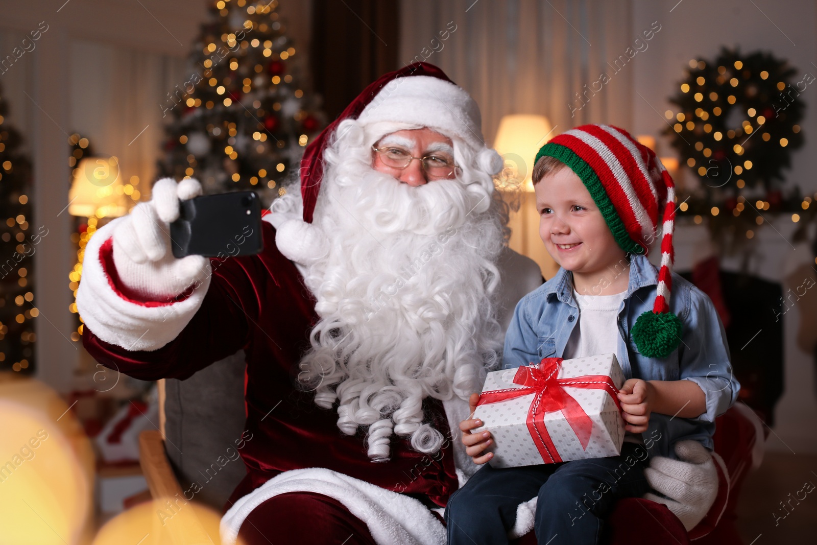 Photo of Santa Claus and little boy taking selfie in room decorated for Christmas