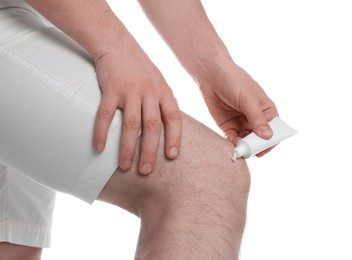 Man applying ointment from tube onto his knee on white background, closeup