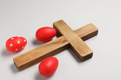 Wooden cross and painted Easter eggs on light grey background